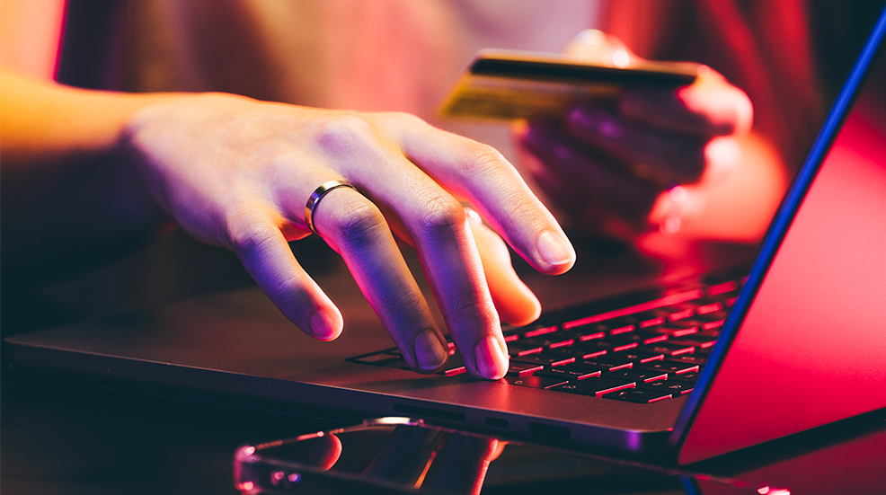 Hands holding a credit card and using a laptop under neon light.